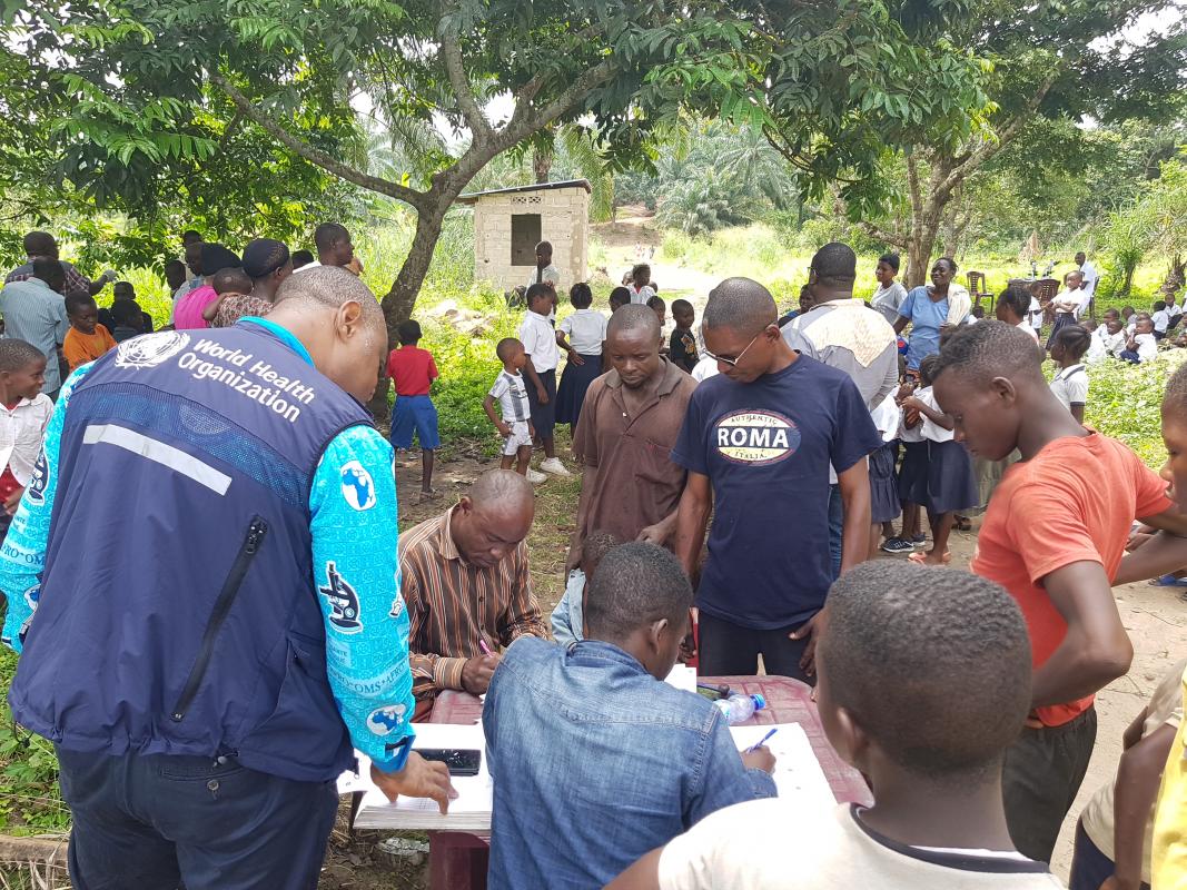 Un expert de l'OMS vérifiant les listes de la première table où l’on convoque les personnes inscrites pour la remise de jeton avec les agents de la surveillance à Lutendele. OMS/Eugene Kabambi