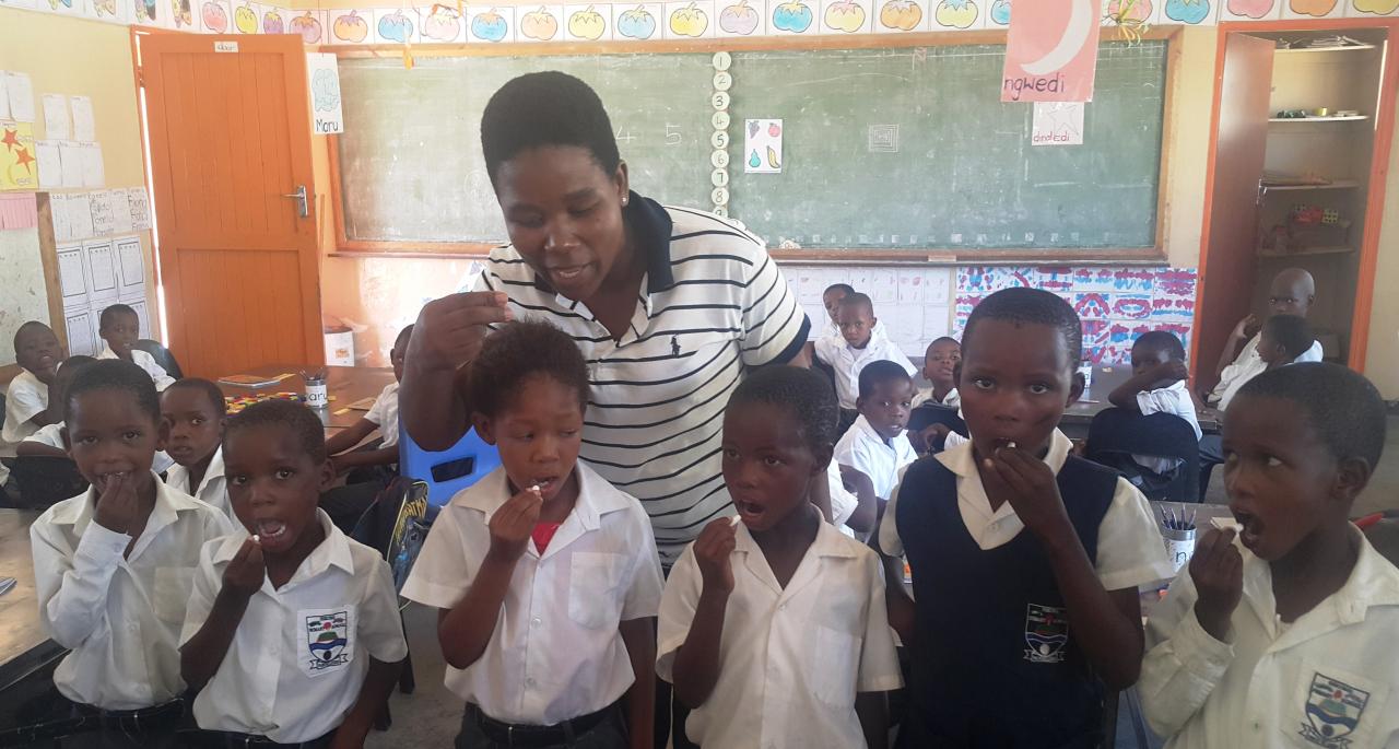 Children being assisted by a teacher to take Albendazole for STHs deworming