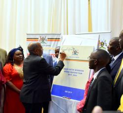 Prime Minister of Uganda Dr Ruhakana Ruganda signs on a dummy copy of the HSIRRP to launch the plan as government officials and partners look on 