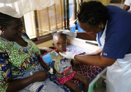 Photo of a nurse attending to Moses while Ebie looks on. The child's health has improved considerably due to the quality of care he received at the hospital