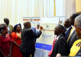 Prime Minister of Uganda Dr Ruhakana Ruganda signs on a dummy copy of the HSIRRP to launch the plan as government officials and partners look on 