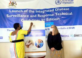 State Minister of Health in Charge of General Duties, Hon Anifa Kawooya signs to launch the IDSR guidelines, while CDC Country Director, Dr Lisa Nelson looks on.