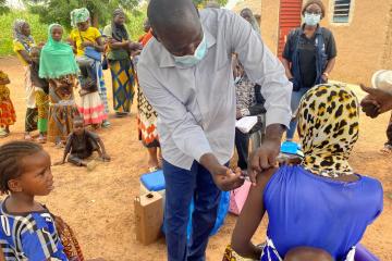 A man vaccinating a woman carrying a baby on her back