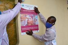 Deux mobilisateurs sociaux de Mbandaka en train de fixer les affiches de sensibilisation pour la campagne près du marché central du chef-lieu de l'Equateur.