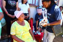 Traditional leader demonstrating how to check for blood sugar with a community member during the house visits